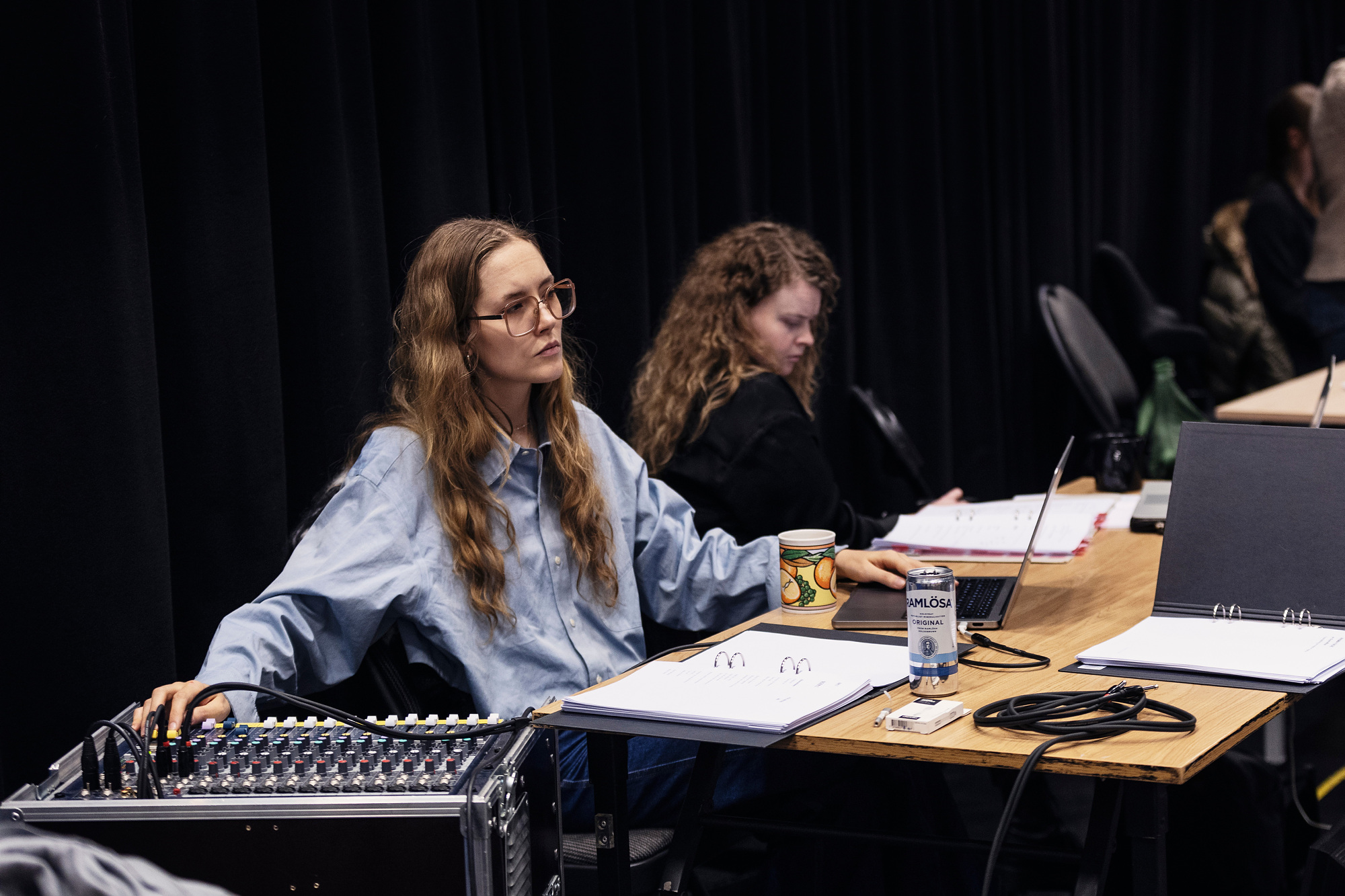 Två personer vid ett bord. Personen till vänster har ena handen på en ljudmixer-bord.