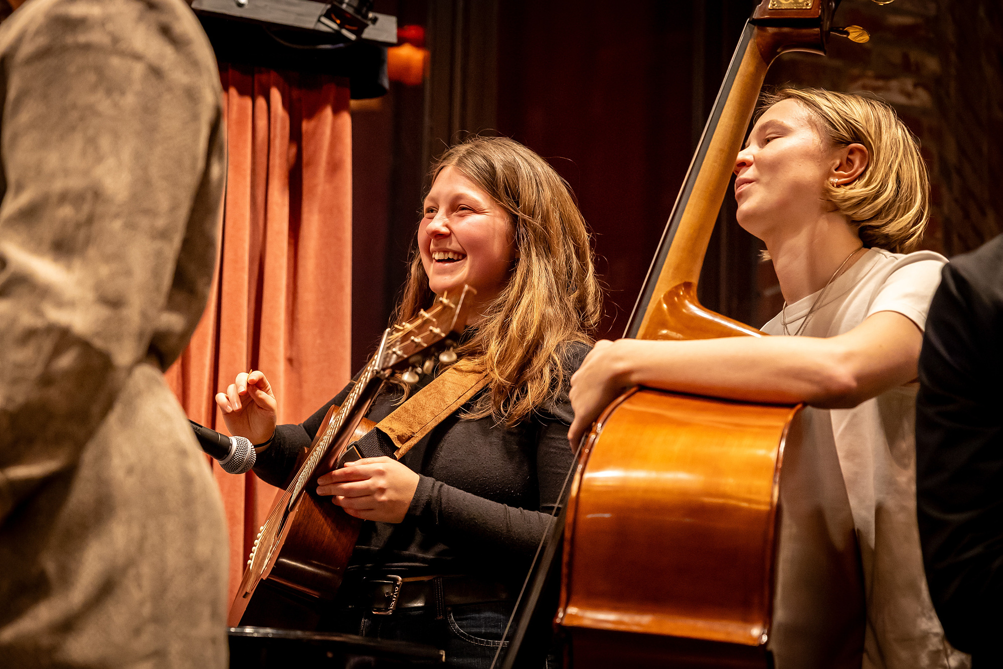 En musiker spelar akustisk gitarr bredvid en kontrabasist, båda ser glada ut.