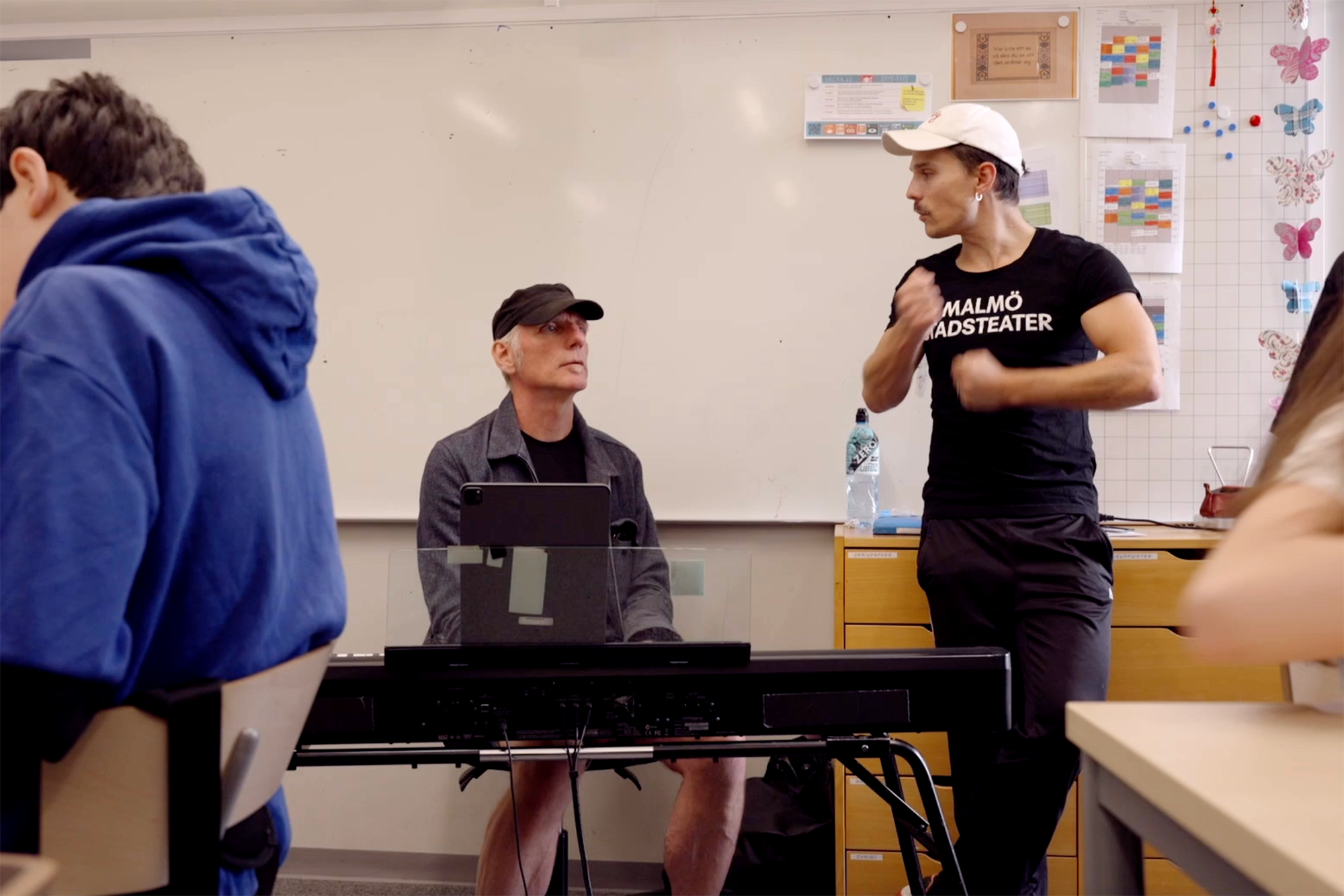 En peron vid elektrisk piano, en annan står bredvid med Malmö Stadsteater tshirt och instruerar med armarna.