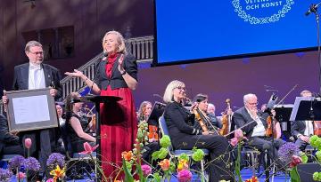 Prisutdelning på en scen. Två personer på förscenen. Orkester i bakgrunden.