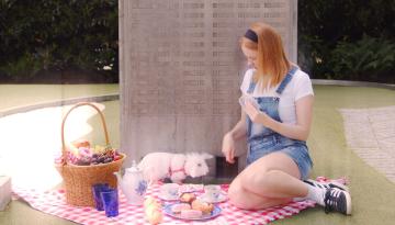 En flicka sitter på en rödvit duk, med picknickkorg, uppdukat fika tillsammans med en vit kanin
