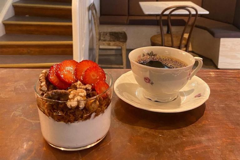 Yoghurt i glas toppad med granola, valnötter och jordgubbar. Kaffe i blommig kopp