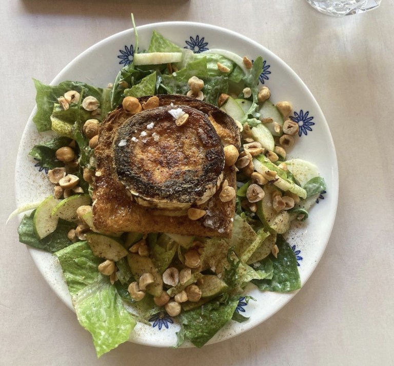 sallad med chevre chaud, äpplen, hasselnötter. Blåvit porslinstallrik på vitlaserat träbord