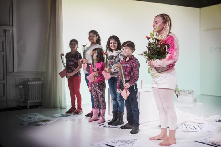 Skådespelaren och de medskapande barnen står på scenen med blommor i händerna och tackar för publikens applåder.