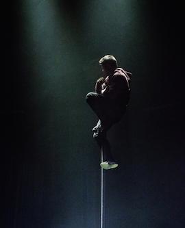 Artist sitter fastklamrad vid en stång högt upp i luften