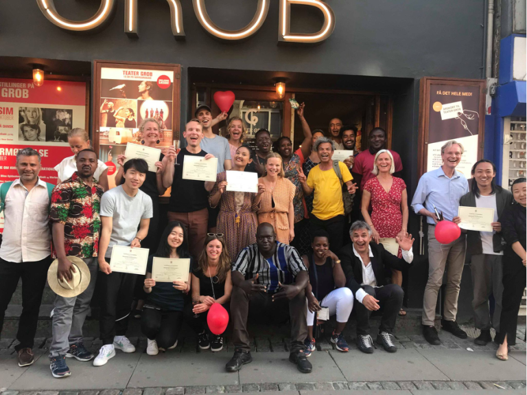 Gruppbild med alla Prospero Workshops deltagare som står framför en teater i Köpenhamn och håller vart sitt diplom i handen.