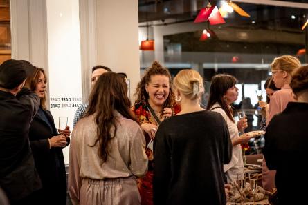 Folk som minglar i teatercaféet. En person i röd tröja står och skrattar tillsammans med två personer som vänder ryggen till mot kameran. 