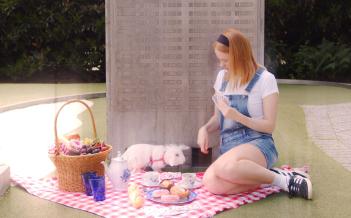 En flicka sitter på en rödvit duk, med picknickkorg, uppdukat fika tillsammans med en vit kanin